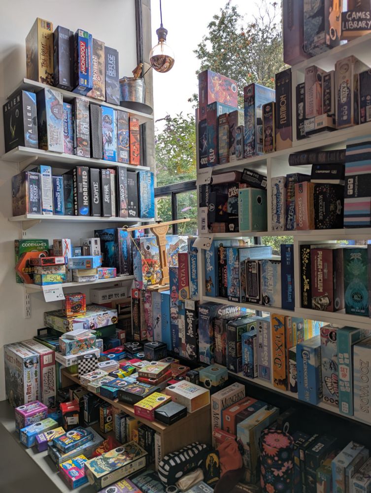 The board game café Ancient Robot Games board game library of games available to play in store. There are shelves of board games by a window.