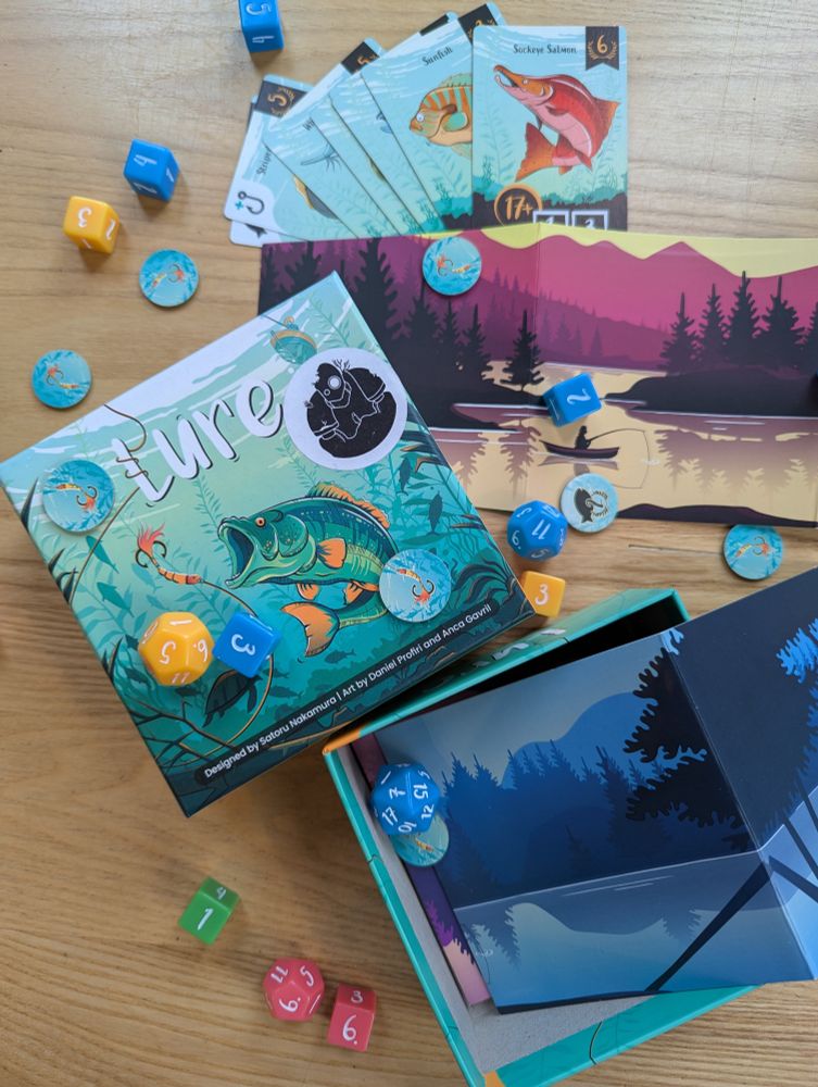 The board game Lure with a picture of a fish on the cover. There are different colour dice, tokens and cards with illustrations of fish.
