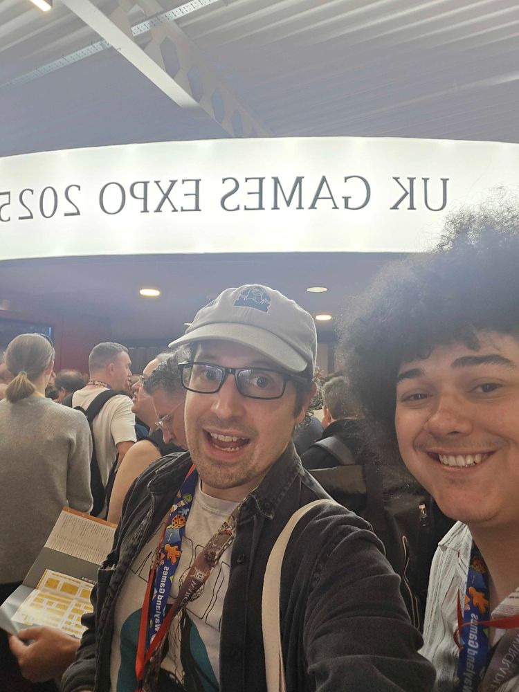 Ancient Robot Games board game shop staff members smiling under a sign saying UK Games Expo 2025.