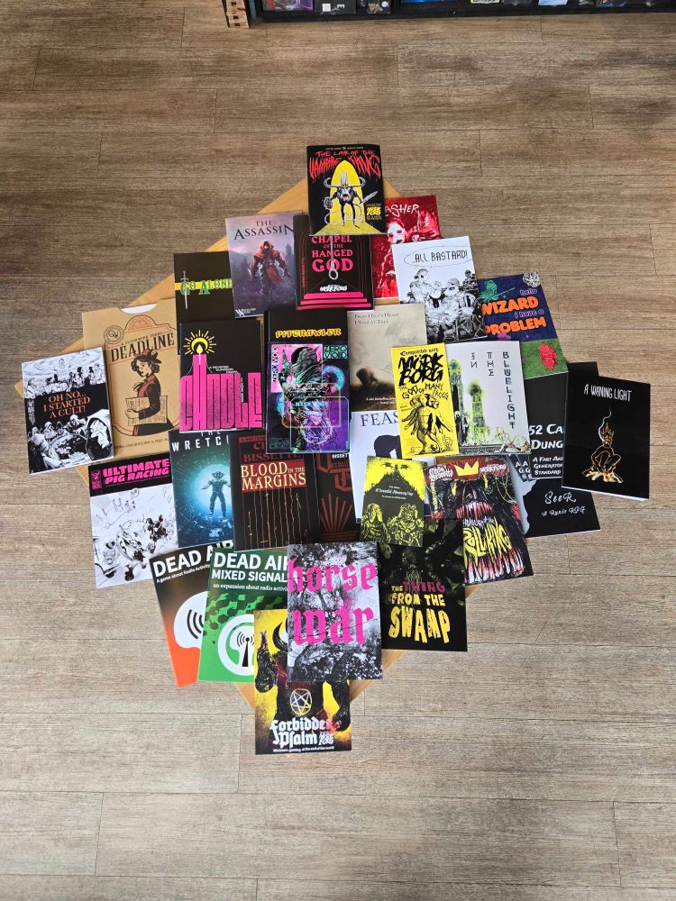New RPG zines layered on top of each other on a table in the Edinburgh board game shop Ancient Robot Games.