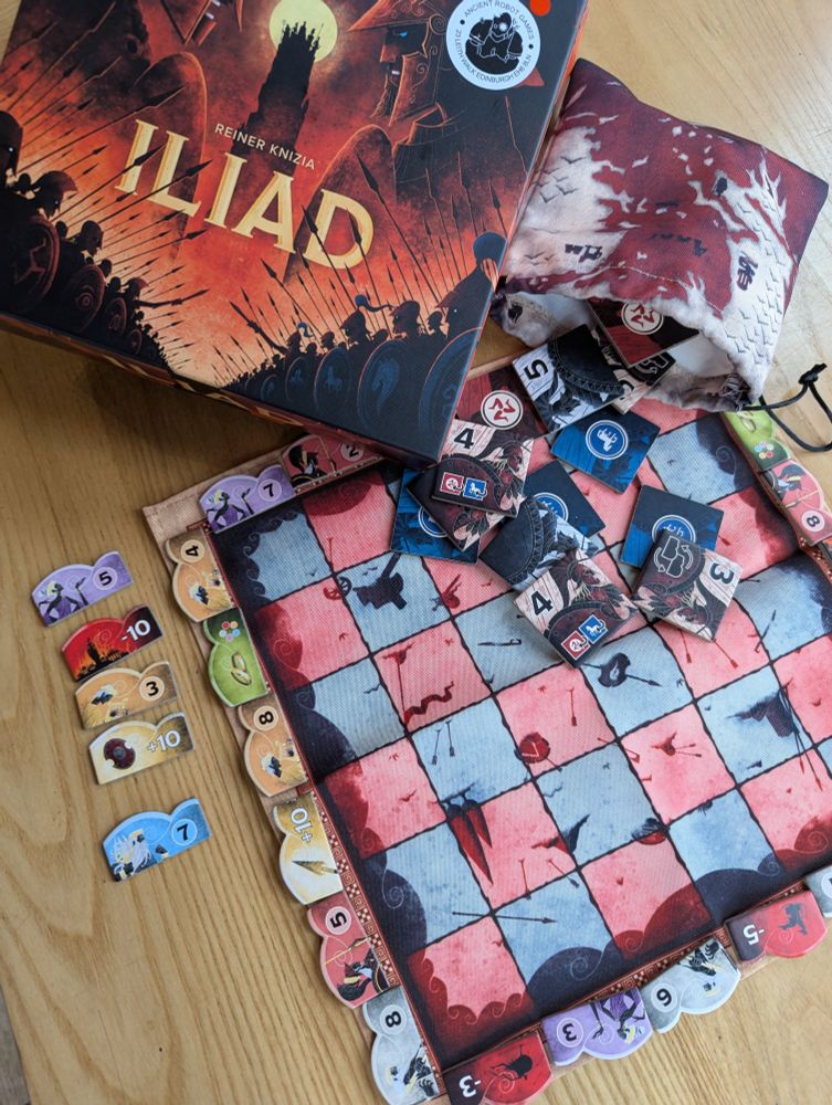 The board game Iliad on a table in the Edinburgh board game cafe Ancient Robot Games. The game has a canvas mat, score markers with different colours and tile pieces