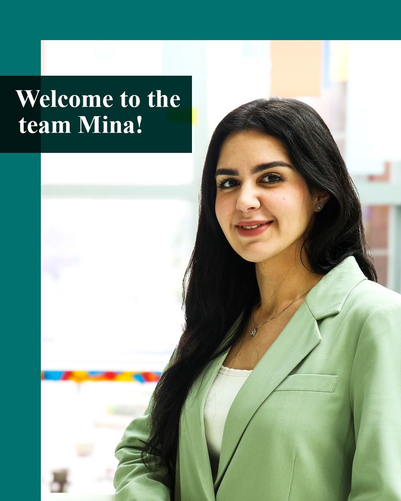 Image consists of a photo of a smiling person with long, dark straight hair. They are standing inside, wearing a light green jacket over a white top and necklace. There is a green border and text inset on a green box reading Welcome to the team Mina!