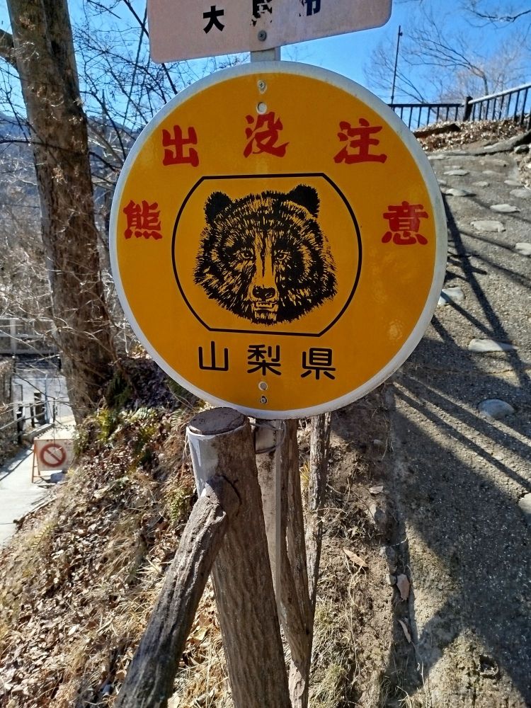 An orange panel representing a bear's head. The text ahead, in red kanjis, seems saying tonthe visitor to be attentive at the presence of bears (according to Google Lens).