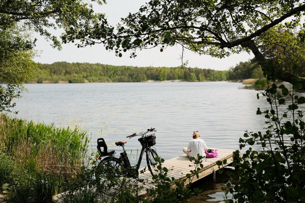 Woman sitting by the water with her bicycle parked nearby on a summer day in Stockholm, Sweden.