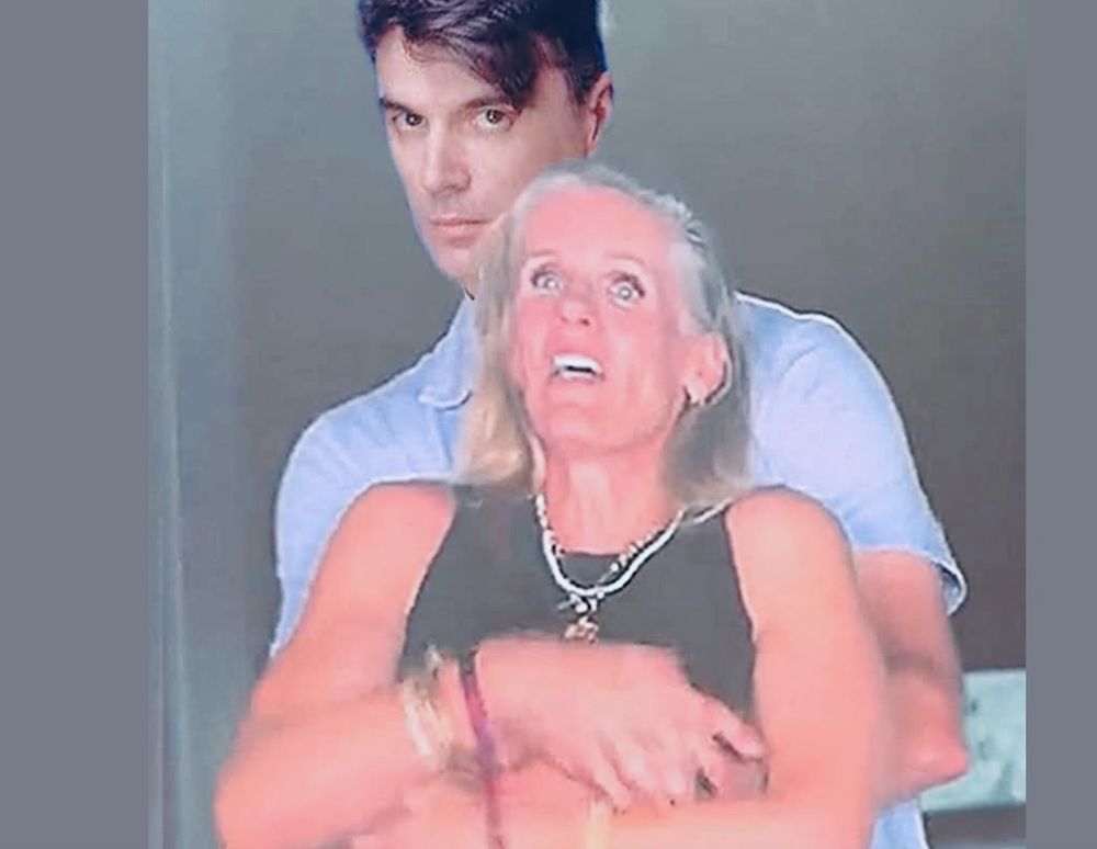 A photoshopped version of a still from the now-infamous kiss-cam shot of the Astronomer CEO & his HR mistress, caught in an embrace... except this one has a young David Byrne circa 1980 - think "Once In A Lifetime" - "THIS IS NOT MY BEAUTIFUL WIFE!" That's one of the lyrics from the song. remember?
"... And you may ask yourself, "How do I work this?"
And you may ask yourself, "Where is that large automobile?"
And you may tell yourself, "This is not my beautiful house"
And you may tell yourself, "This is not my beautiful wife!" 
Yes, that's right, I'm explaining the joke. Why? Because as a moderately neurodivergent person, I often find myself missing the joke & feeling stupid, so I don't like to think about OTHERS possibly missing the joke & feeling stupid - be they neurodivergent or not - maybe just not familiar with the material. Hence... the explanation. You're welcome. 