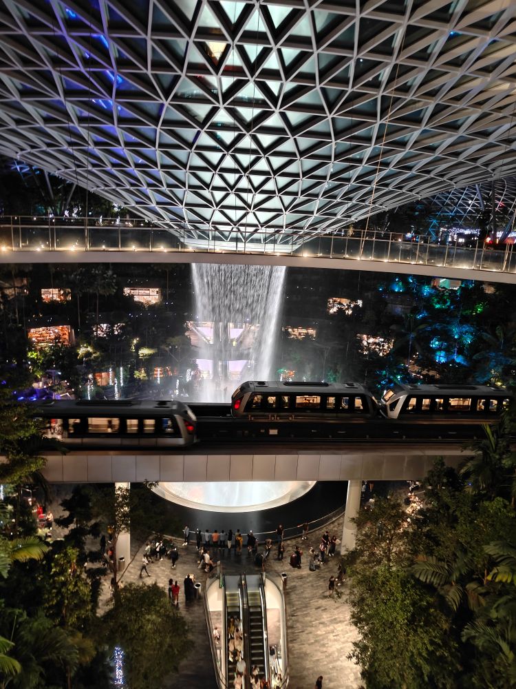 night time photograph of the airport in singapore with a water fountain and trains