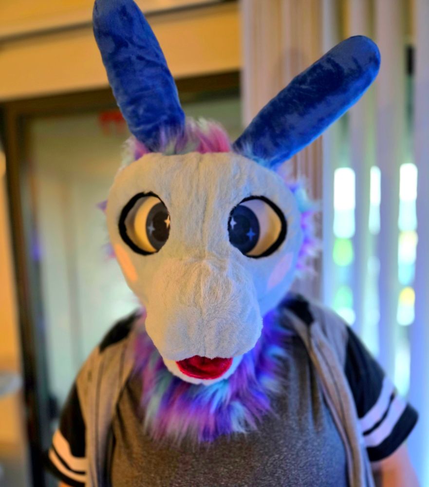 Rainbow fish crossed with a dragon fursuit has blues and purples and pinks