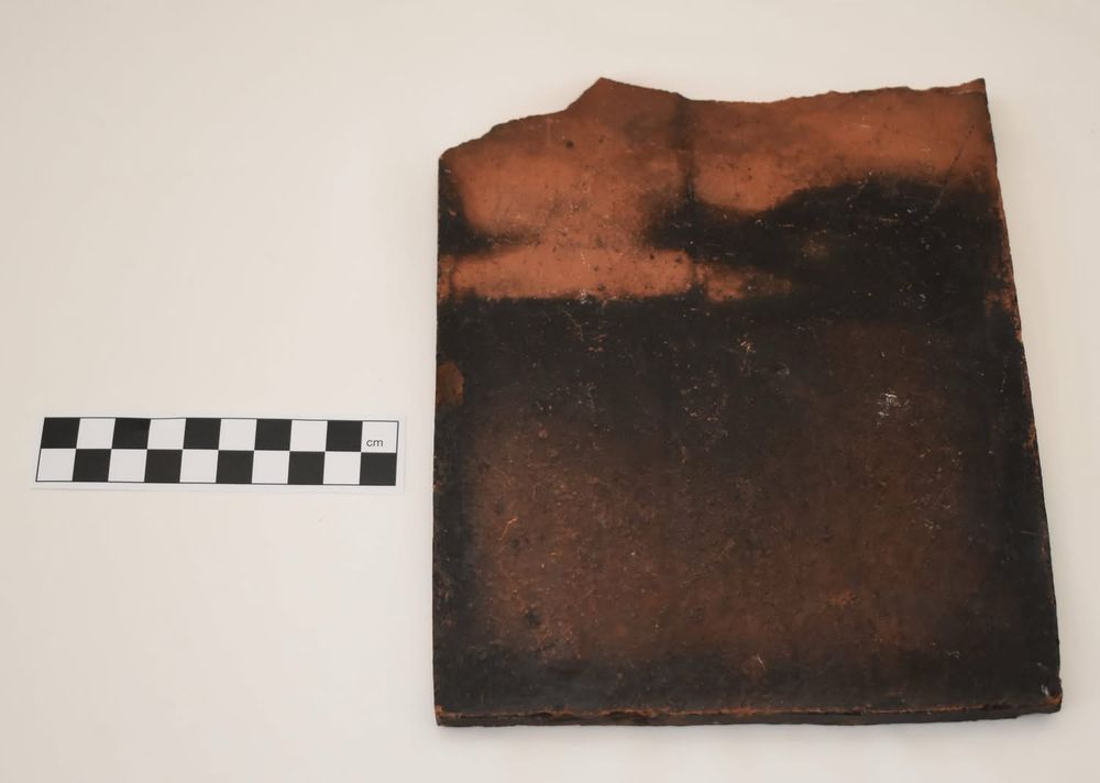 A terractotta tile with the lower half blacked by soot smoke on a white table top.