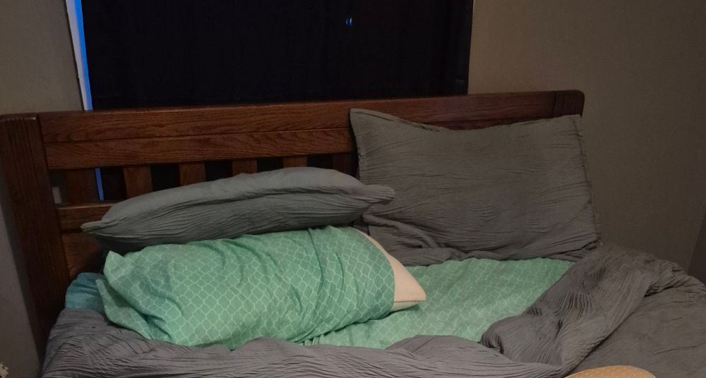 Picture of a bed, with blankets pulled down from the headboard in the center and the pillows knocked over.