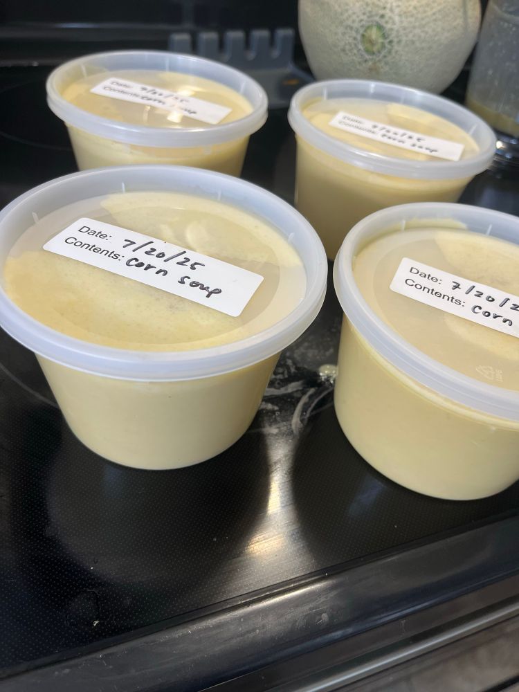 Four two-cup deli containers of purées corn soup, a light yellow liquid with labels