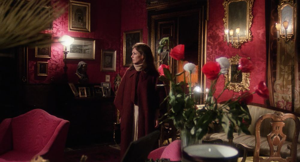 Jennifer O'Neill dans un salon ancien aux couleurs rouges , roses au premier plan