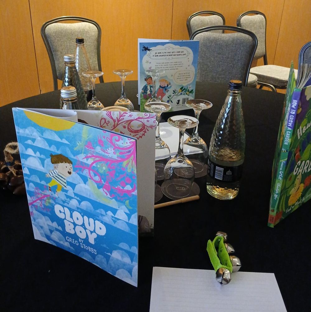A table with three different books sitting on it, a selection of glasses and water bottles.