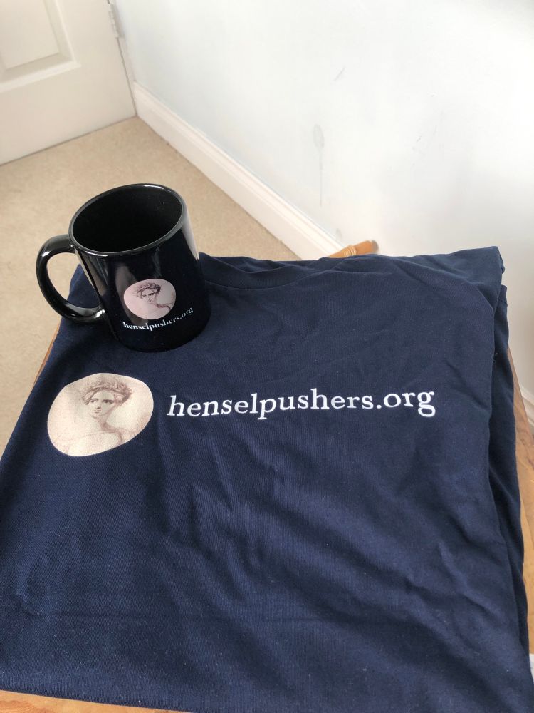 Photo of navy mug and T shirt on a small wooden table, cream carpet and white door visible. The merchandise has a small picture of Fanny Hensel; and the T shirt has Henselpushers.org in white letters across the front