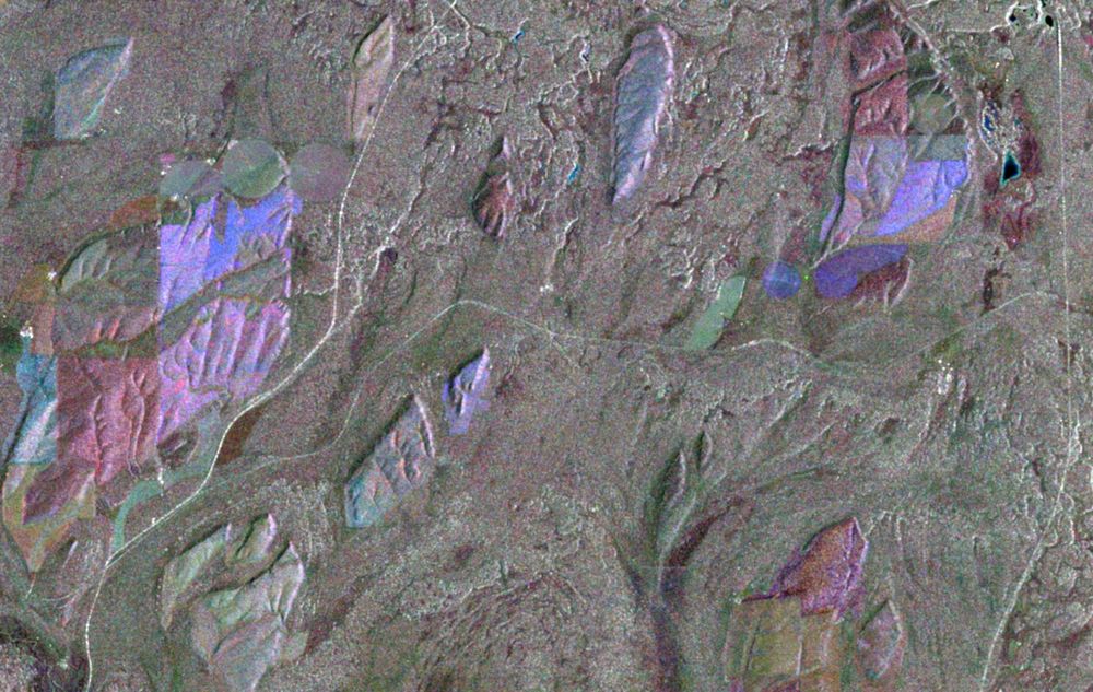Radar-based satellite image showing streamlined oval to irregularly shaped hills of loess standing above flood-eroded basalt. The basalt is gray, but there are light blue, pink, and red tones on the loess.