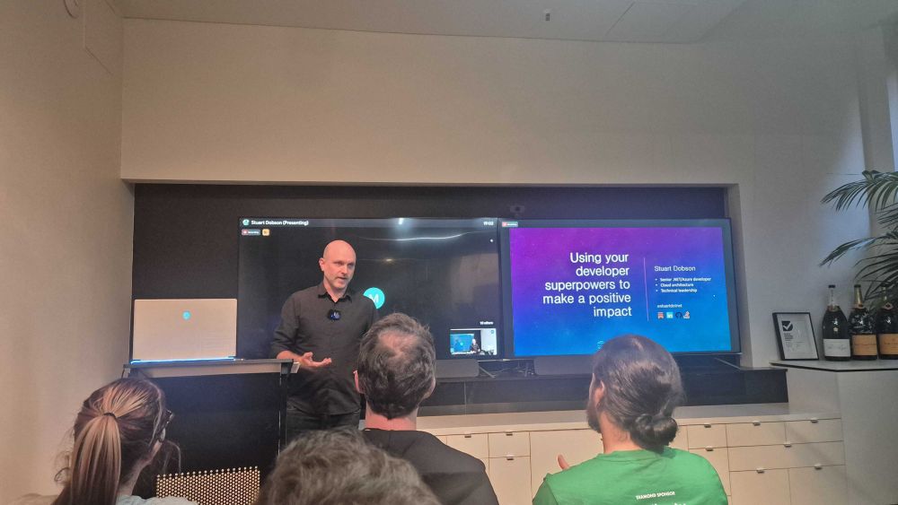 Stuart Dobson stands next to his slides titled "Using your developer superpowers to make a positive impact"