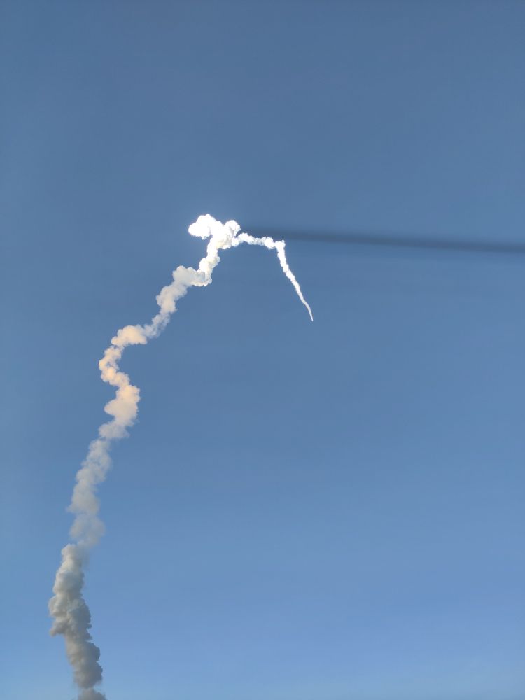 En rökpelare sträcker sig upp i skymningen och når så högt att solen skiner på den. Där är den bländvit och kastar en mörk skugga över himlen.