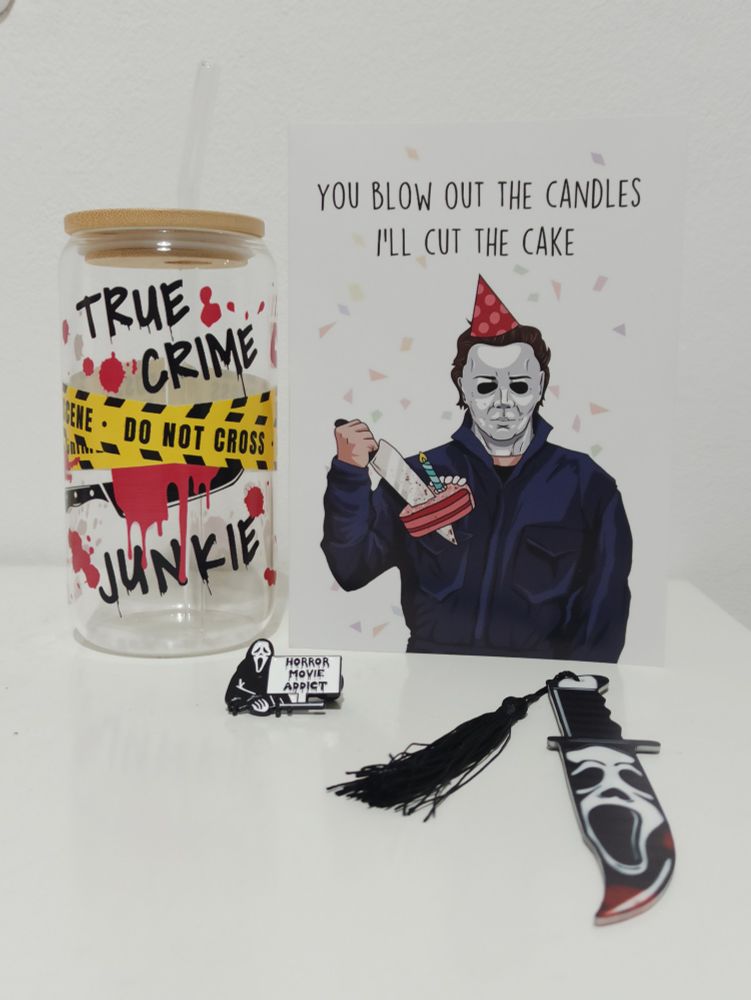 Vaso con texto que pone True Crime Junkie, una postal de Michael Myers, un pin de ghostface que pone horror movie addict y un marca páginas en forma de cuchillo con la cara de ghostface.