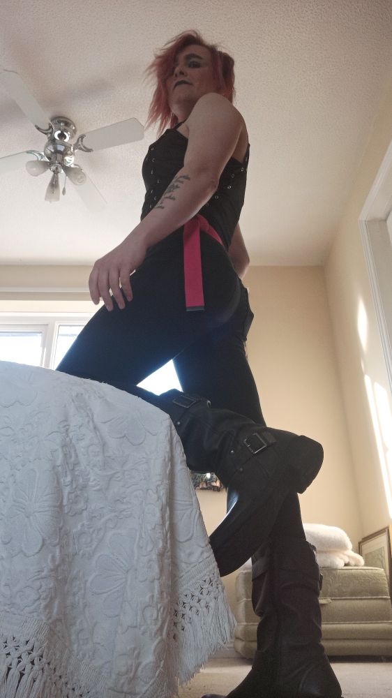 I'm dressed all in black, tight jeans, tight top with a pink belt. My hair is beautifully messy and I'm looking down at you, where you belong. I've got a knee on the bed expectantly, which also shows off my boots