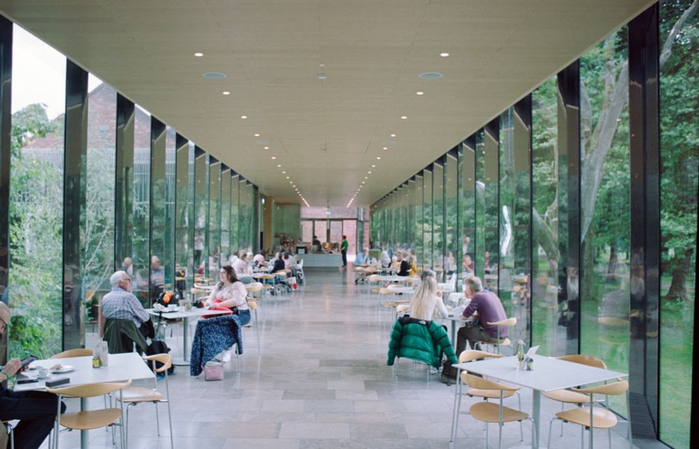 Long, minimalist interior with cafe tables, glass walls at either side, plain ceiling