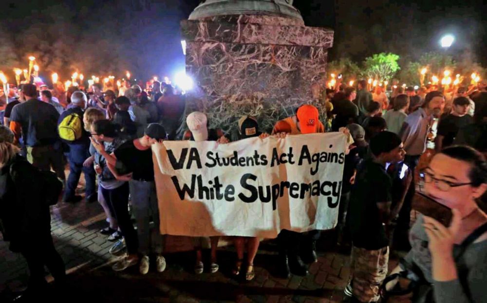 A few students holding a banner reading "Virginia students act against white supremacy," surrounded by torch-bearing fascists and Klansmen.