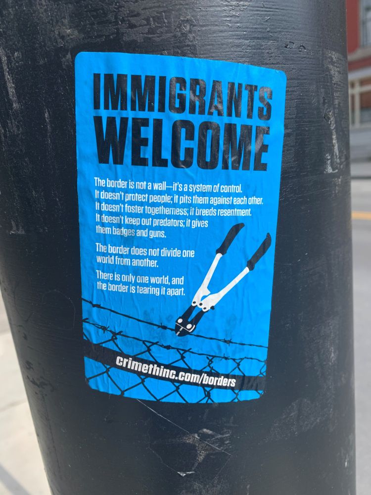 A sticker reading "Immigrants welcome" with an image of boltcutters cutting barbed wire on a pole.