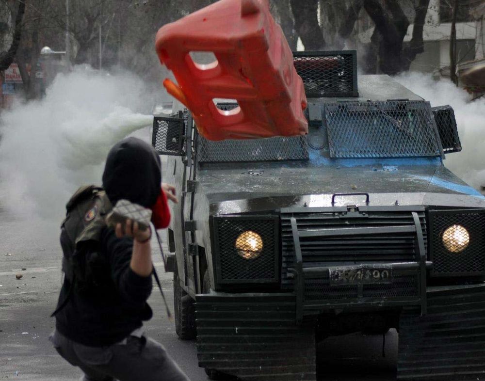 A Chilean student throws a projectile at an armored police car.
