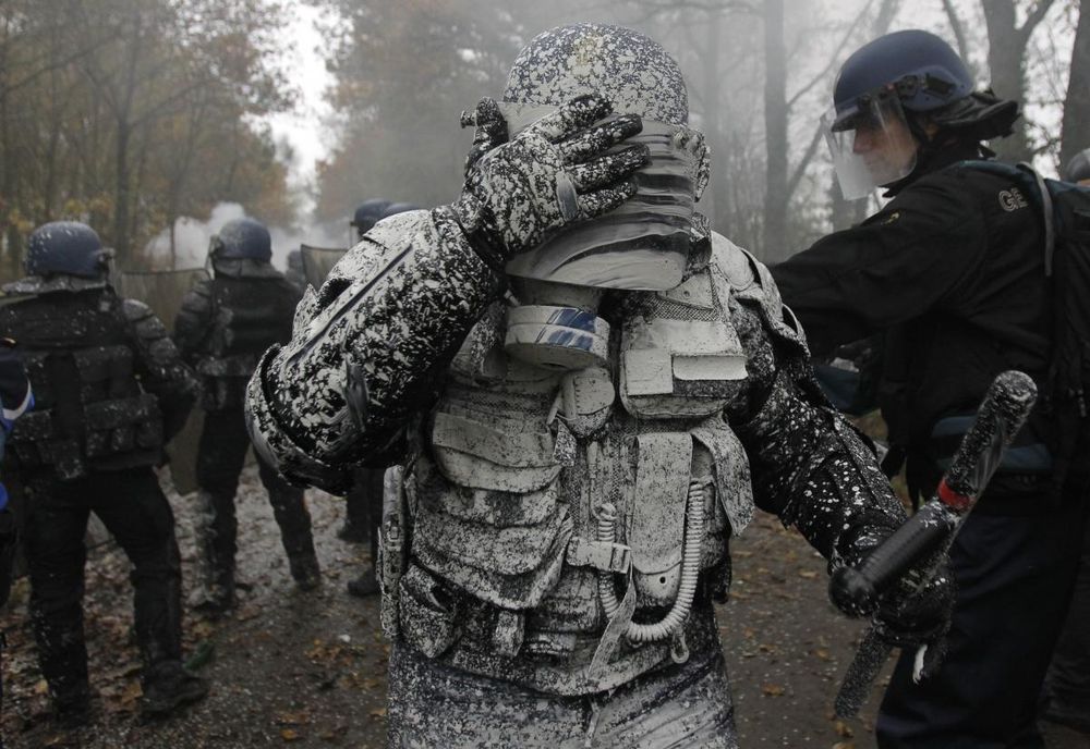 A photograph of a police officer in riot gear, blinded by mud, during clashes at la ZAD, an autonomous zone in France.