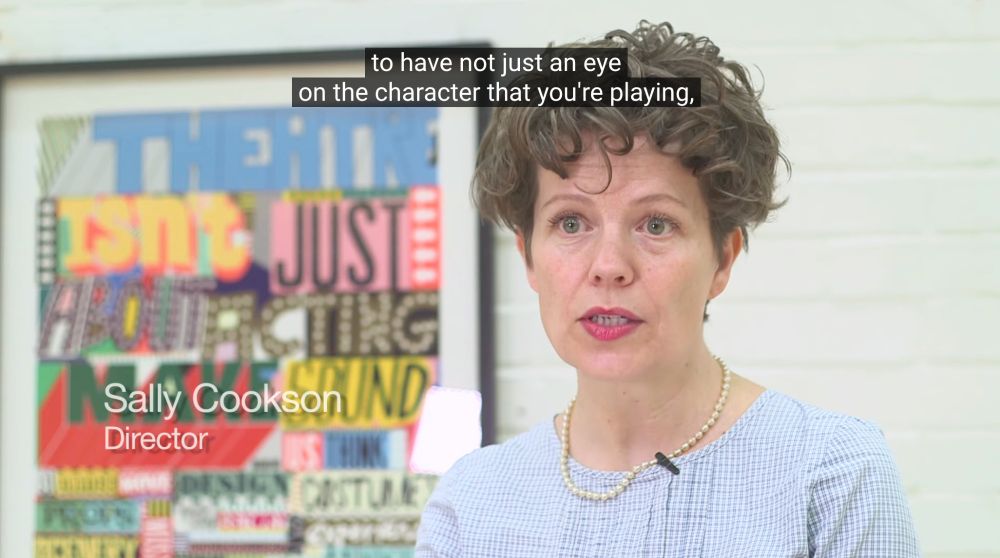 A woman identified as Sally Cookson, the director, is being interviewed in front of a colorful poster. The text on screen reads, "to have not just an eye on the character that you're playing."
