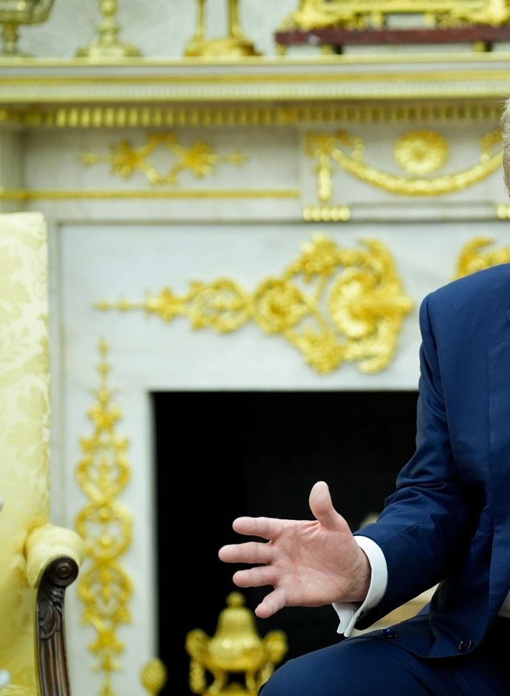 Blurry Oval Office fireplace (in background) from July 2025 that shows that gold now covers more of the existing features on the fireplace, including the dentil trim.