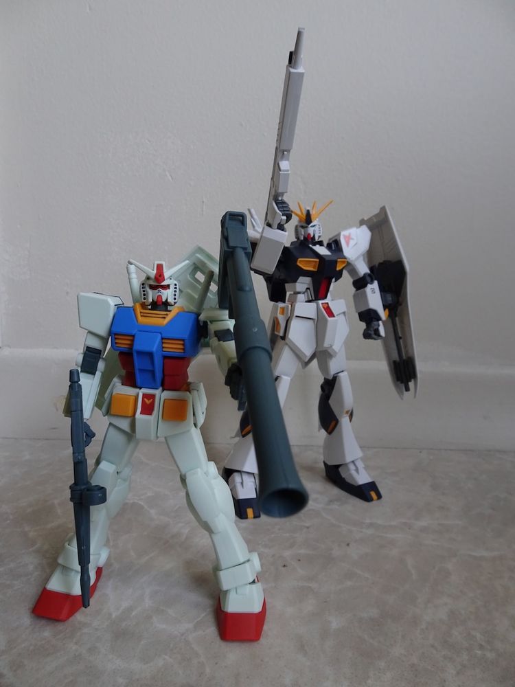 Two 1/144 Gundam model kits. The smaller one in the front has had its head detailed with a marker and then been sprayed with a flat top coat.