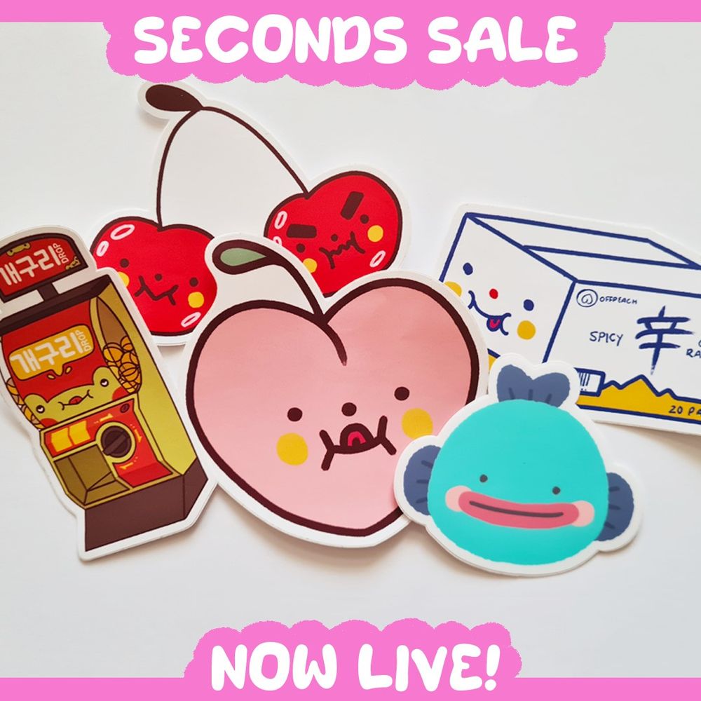 An assortment of cute illustrated stickers with the text "Seconds sale now live!" at the top and bottom. The text is white on on bright pink clouds. From left to right, the stickers are of a frog themed gacha machine, a pair of cherries with different expressions, a peach with a cheeky face, a fish OC called Boni, and a white and yellow ramen box.