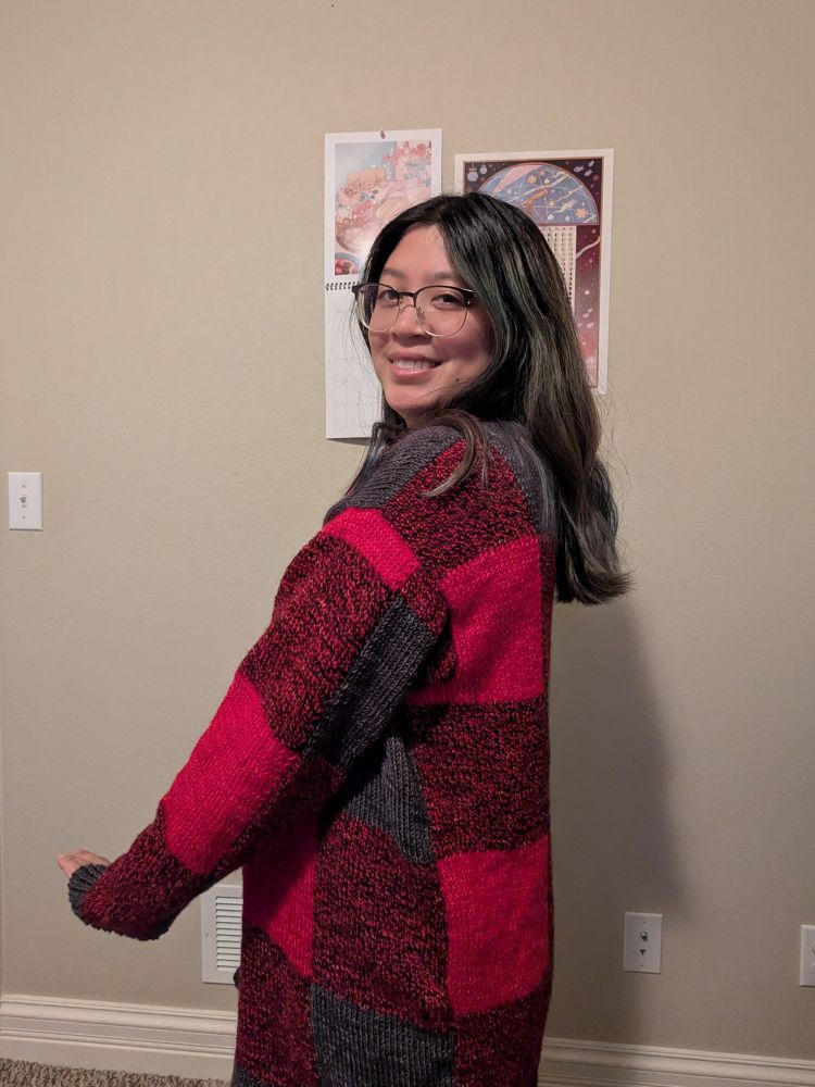 An Asian woman wearing a Caladium Cardigan, which is a plaid-like pattern in red and gray.