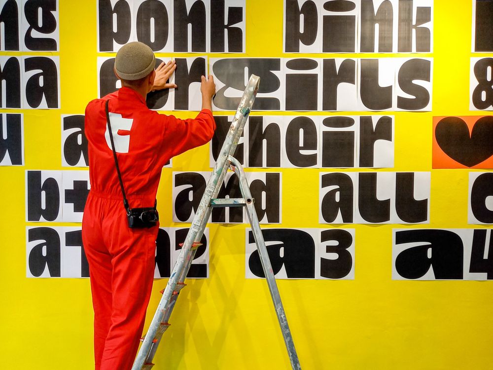 Assembly image from Dina Chaumont’s launch showing lettering being mounted onto a wall behind a ladder.