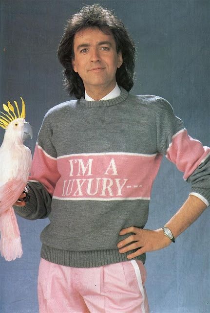 A man wearing a gray and pink sweater that says "I'm a luxury..." 