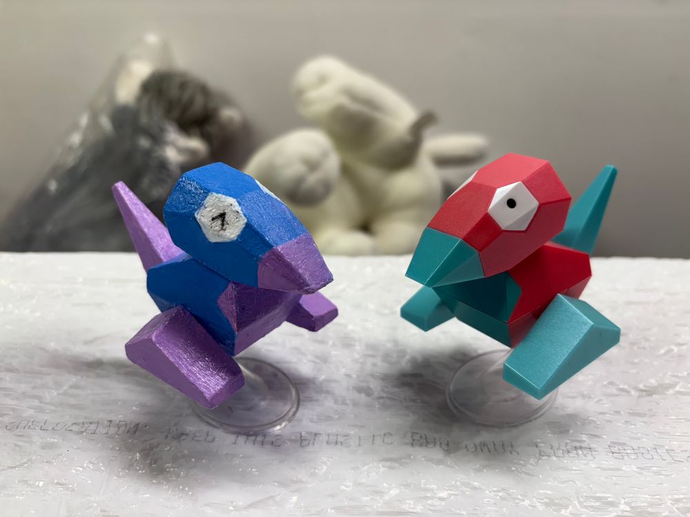 picture of a porygon pokemon figure painted to have it’s shiny color palette, now with a coat of mod podge on her, sitting next to a normal porygon figure. 