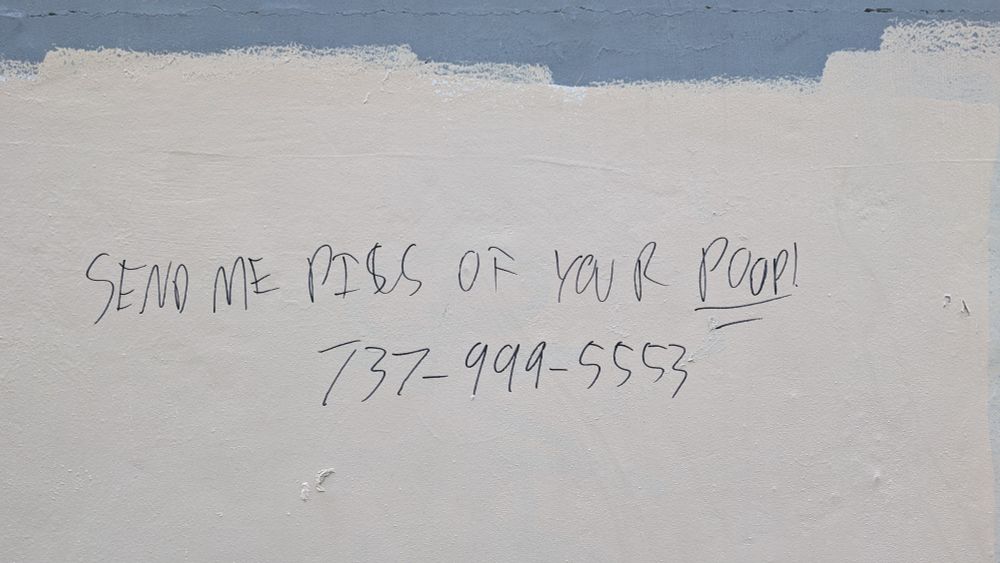 A picture of crude graffiti that says "send me pics of your poop" with a phone number 
