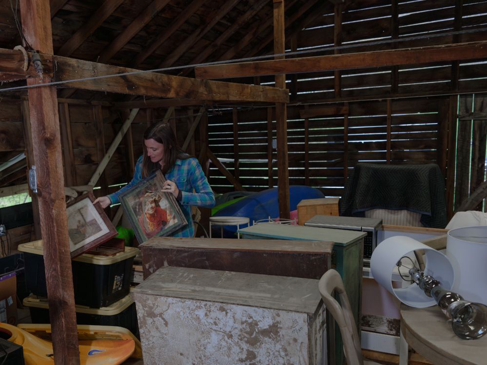A woman holding framed photos while standing among belongings recovered from flooding.