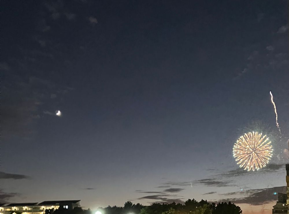 White fireworks by the crescent moon at sunset.