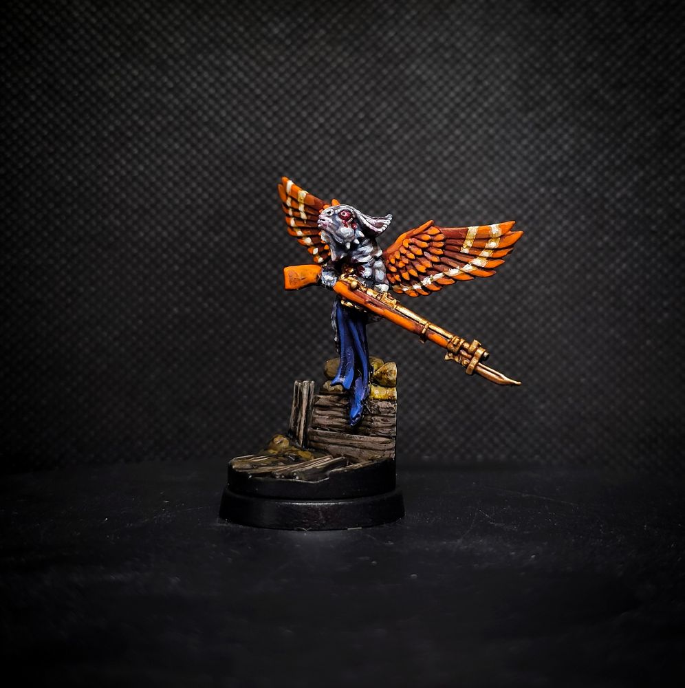 Photo of a kitbashed Takwin Homunculus miniature for Trench Crusade. A cherubic baby with orange hawk wings and the head of a chameleon flies over a trench, hefting a bolt action rifle with obvious effort
