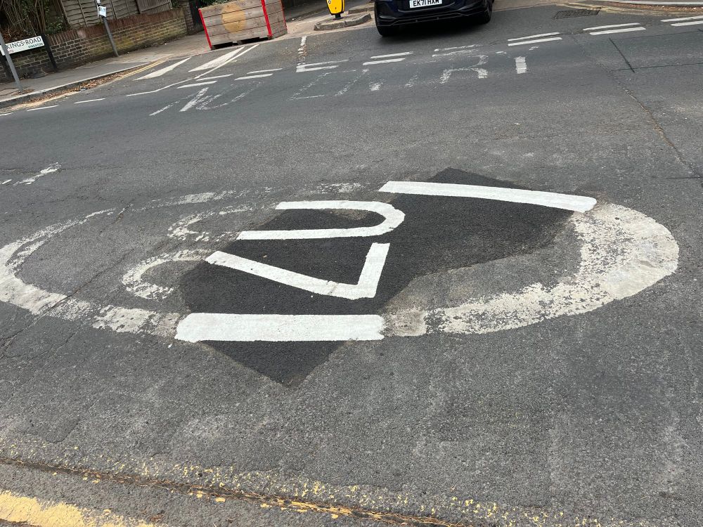 20 in a circle painted on the road. The middle has been repainted, top and bottom left unpainted and very worn. 