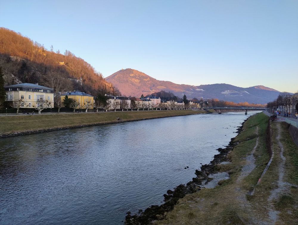 View across the Salzach river in Salzburg, housing on the left hand bank of the river and hills in the distance.