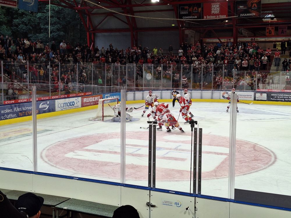 Ein Eisstadion mit Eishockeyspielern auf dem Eis, die Richtung Tor fahren. Ringsum Zuschauer.