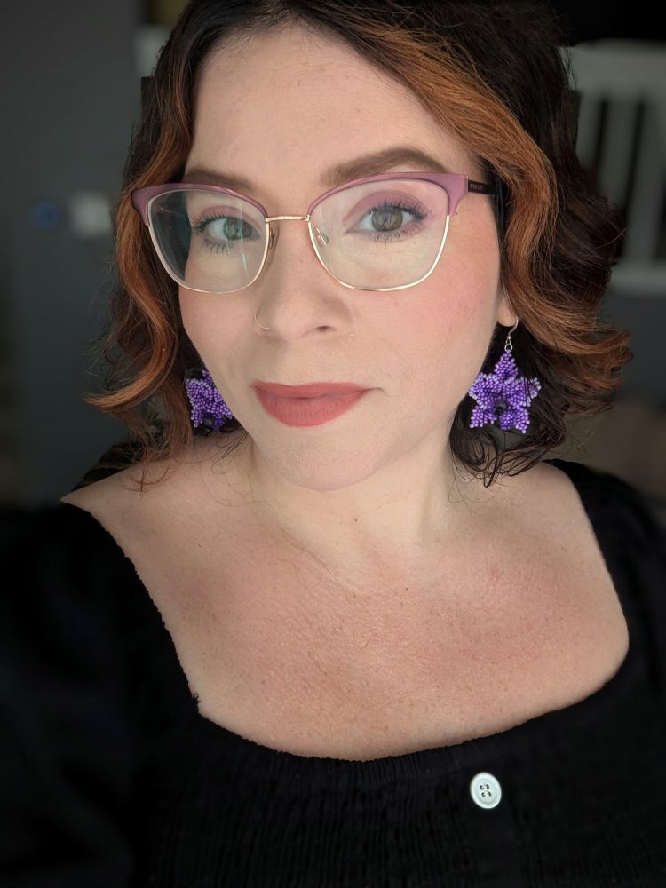A photo of me (reddish hair, glasses) wearing purple beaded earrings and a black dress. 