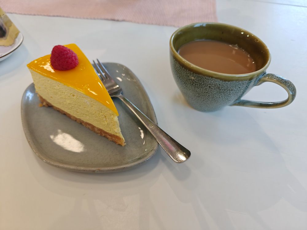 Gluteeniton ja vegaaninen mangojuustokakun pala sekä kuppi kahvia. 