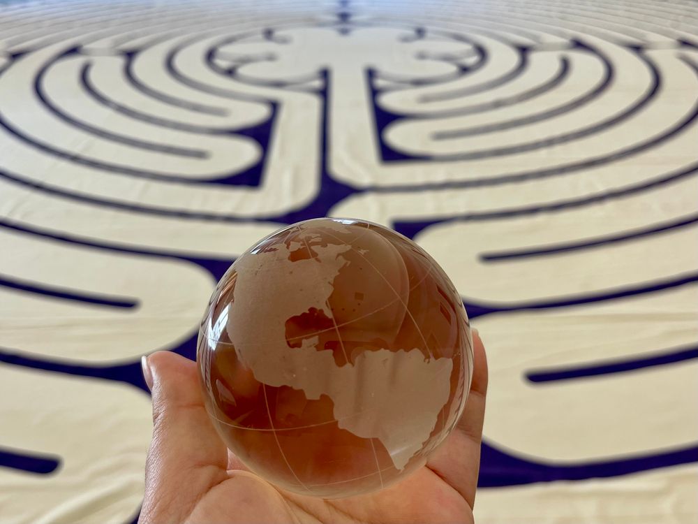 Photo of a large Chartres style labyrinth on canvas with an outstretched hand that holds a crystal ball replica of earth. Says, Sacred path and winding road led me back to myself today. Head up. Shoulders back. Resolute. Guided by love and wisdom. I was born for these times. So were you.