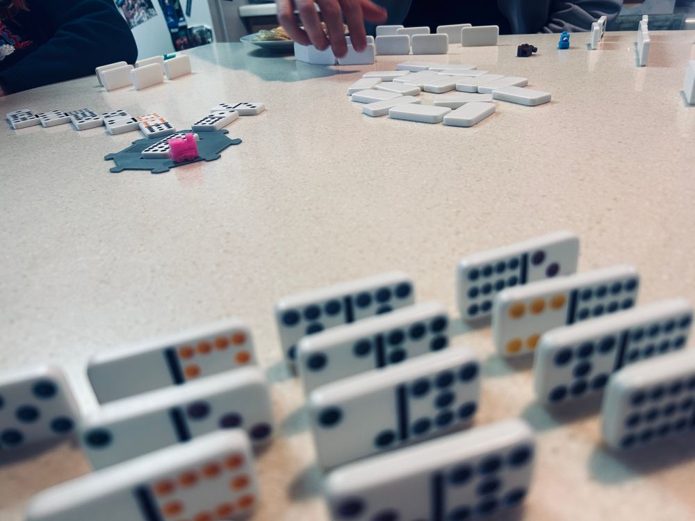 Table with dominoes and trains, some dominoes are sitting on their sides for the player to see, others are laid end to end as played game tiles. 