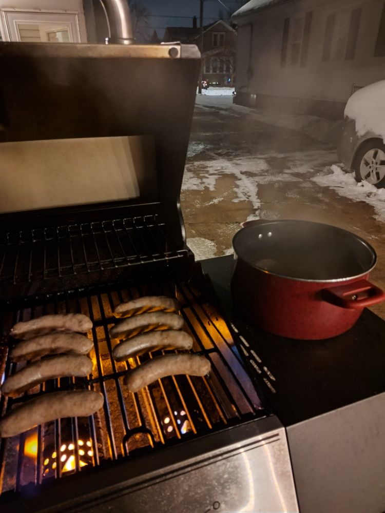 Brats and dogs and sausages on a grill outside in the dark