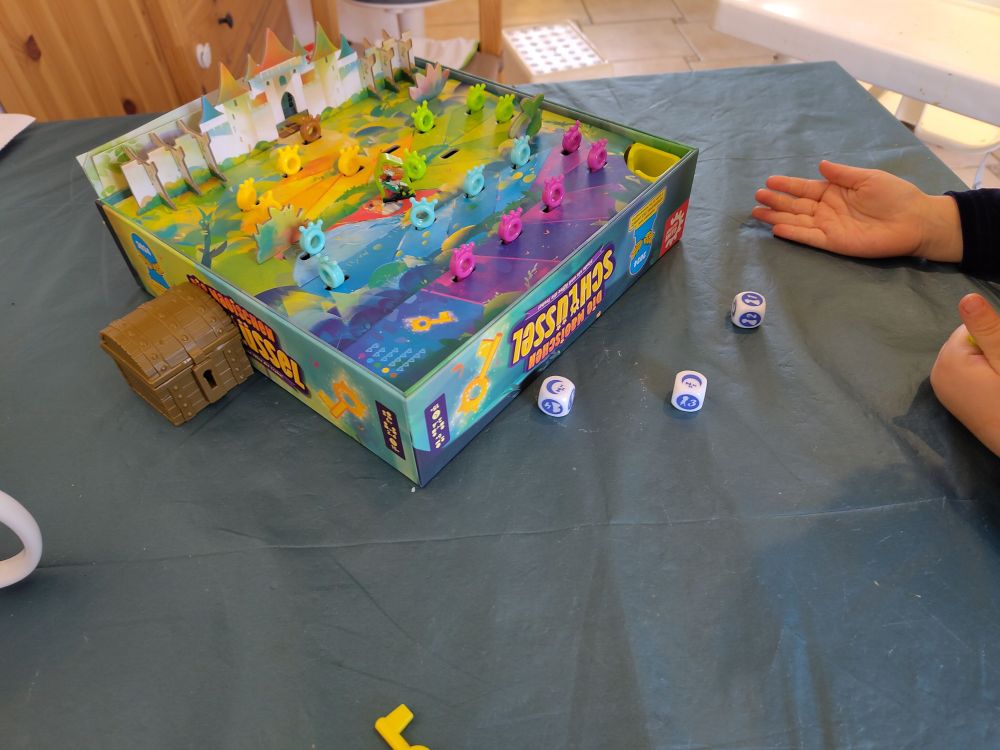 Ein Bild vom Spiel "Die magischen Schlüssel" mit einer Kinderhand daneben.