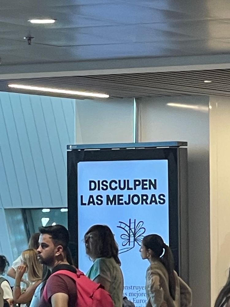 Un cartel en la estación de Chamartín, llena de gente con el AVE con retraso, que dice “disculpa las mejoras”