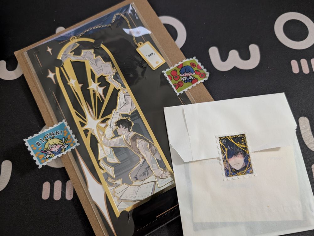 omniscient reader viewpoint gilded bookmark from skradio. a boy with bandages on his face reaches towards a star, with pages fluttering all around him. a chain connects the top of the bookmark to a smaller label with the word, 「■■■」. Next to the bookmark is a freebie envelope